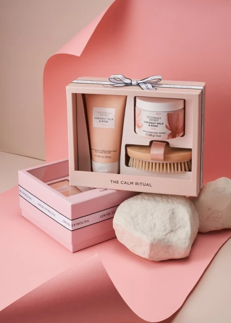 Victoria's Secret Calm Ritual set featuring body scrub, wash, and brush in a box on a pink background, product photography.