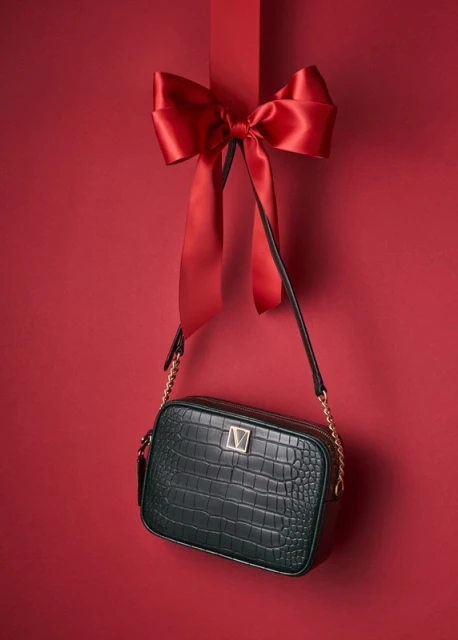 An elegant green faux crocodile purse with a gold chain strap is displayed against a deep red background with a matching red ribbon.
