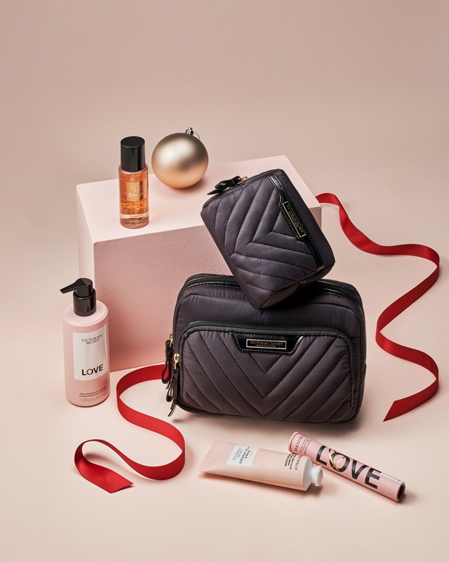 Cosmetics still life featuring gift sets with a pink background, red ribbon accents, and a shiny gold ornament for the holiday season.