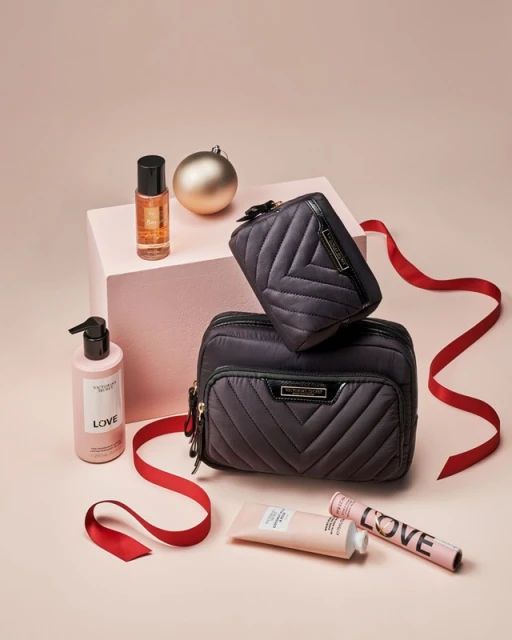 Cosmetics still life featuring gift sets with a pink background, red ribbon accents, and a shiny gold ornament for the holiday season.