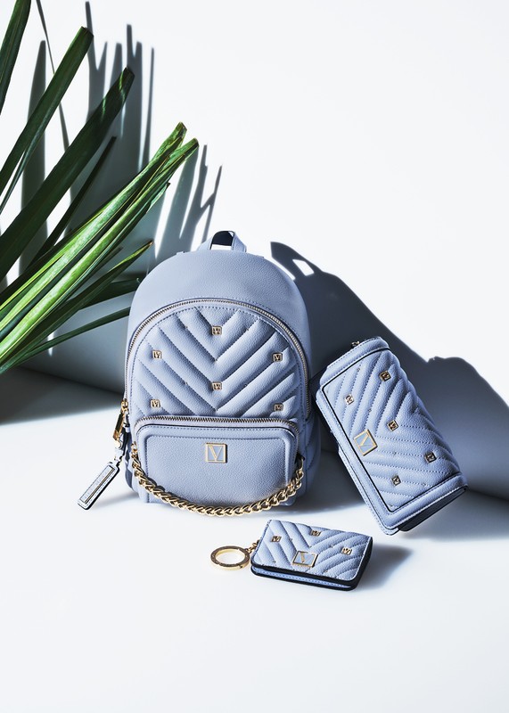 Light blue quilted backpack, wallet, and cardholder accessories set with gold chain, hardware, and leaf shadow in studio.