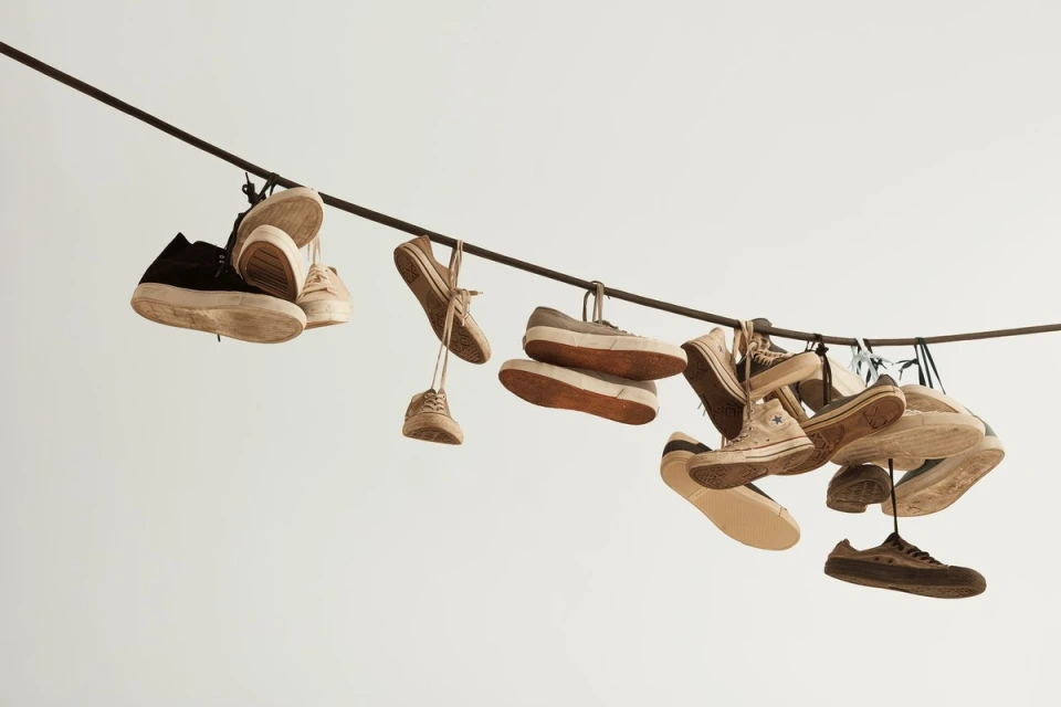 Several worn sneakers hang from a dark wire against a stark white background, creating a minimalist and intriguing composition.