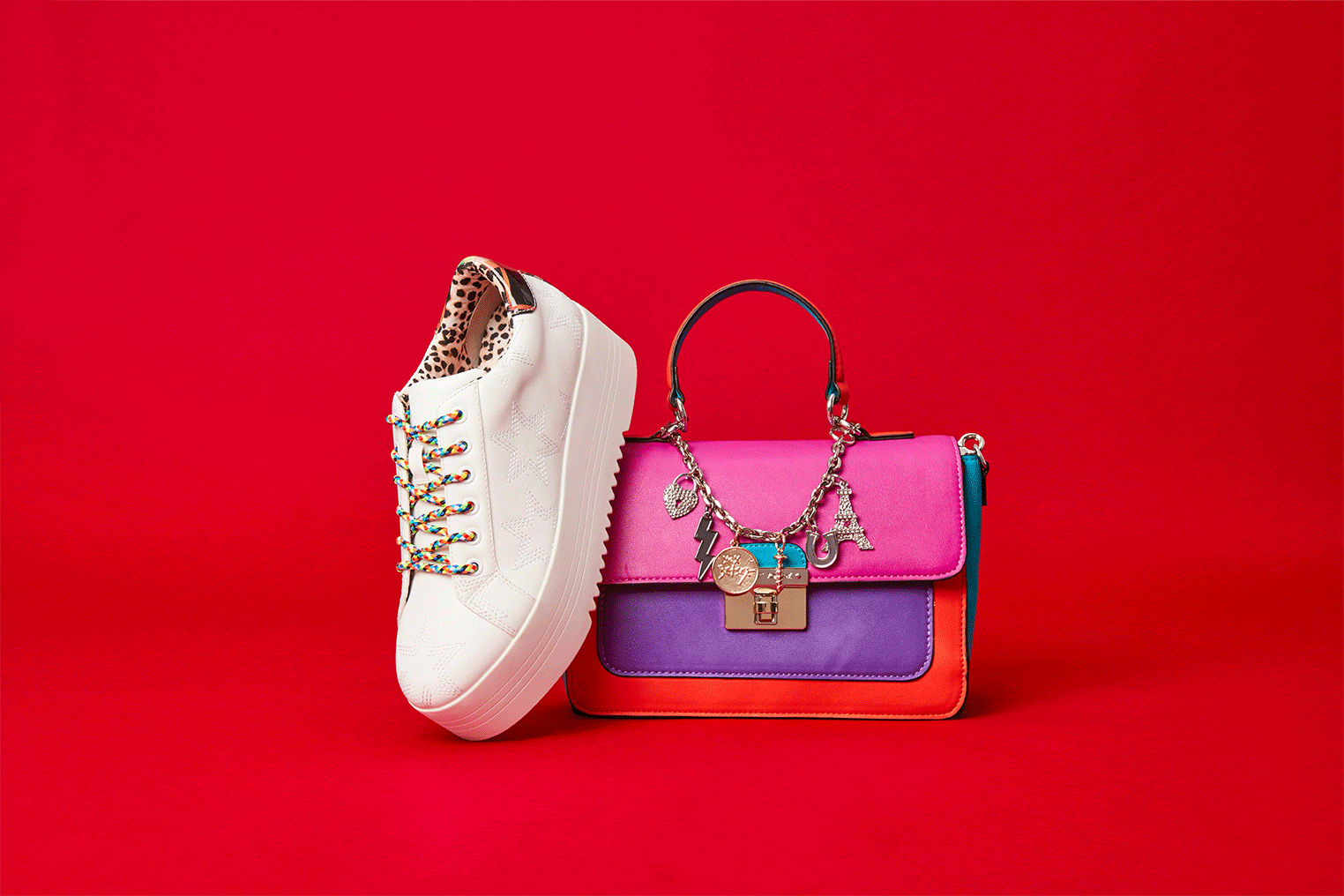 Still life of a white platform sneaker and a colorful small purse set against a solid red backdrop in a studio setting.