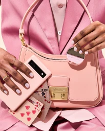 Close-up of pink handbag, smartphone, compact mirror and playing cards styled by prop stylist Rachel Stickley
