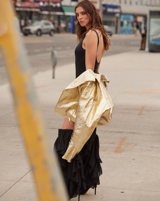 Outdoor fashion shoot featuring a woman in a black leotard and skirt, metallic jacket. Urban setting with cars and buildings.