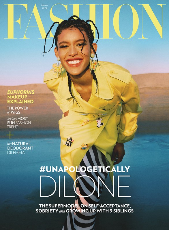 Fashion magazine cover featuring a smiling woman with braided hair wearing a yellow jacket, set against a backdrop of sky and sand.