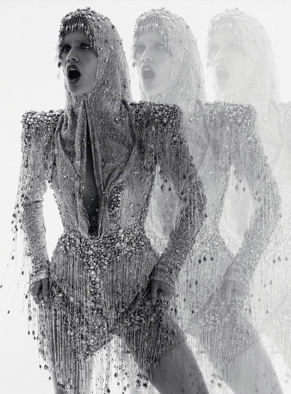Fashion editorial shot of a woman in a beaded hood and bodysuit, captured in a triple exposure effect against a bright white background.