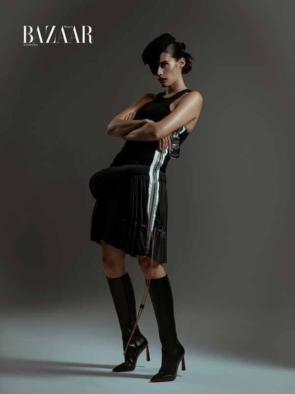 Model in black tank top and pleated skirt with knee-high boots posing in studio