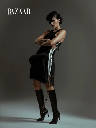 Model in black tank top and pleated skirt with knee-high boots posing in studio