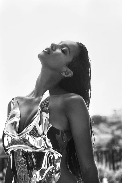 Black and white portrait of a woman in a metallic dress, head tilted back, with an outdoor urban-style background.