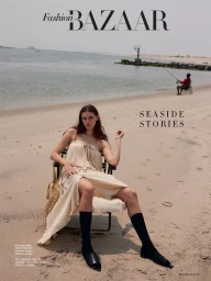 Woman in cream dress and black socks seated on a beach chair styled by Rafael Linares