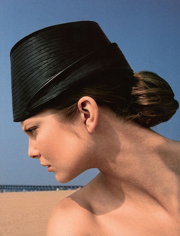 Woman wearing black straw hat at the beach on a sunny day in a fashion style portrait against clear blue sky.