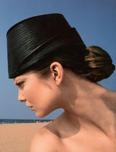 Woman wearing black straw hat at the beach on a sunny day in a fashion style portrait against clear blue sky.