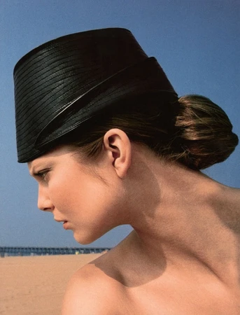 Woman wearing black straw hat at the beach on a sunny day in a fashion style portrait against clear blue sky.