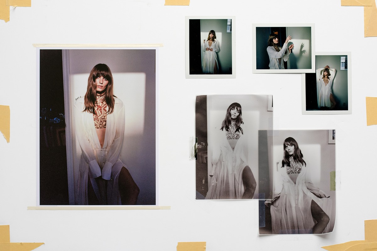 Collage of fashion portrait photographs taped to a white wall, showcasing a woman in a semi-sheer white shirt and patterned crop top.