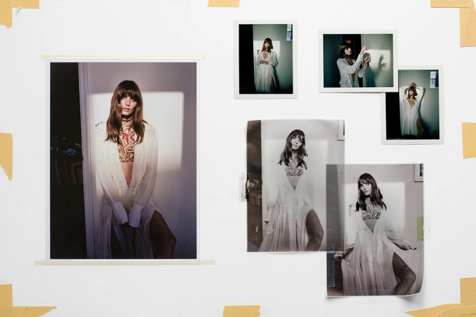 Collage of fashion portrait photographs taped to a white wall, showcasing a woman in a semi-sheer white shirt and patterned crop top.