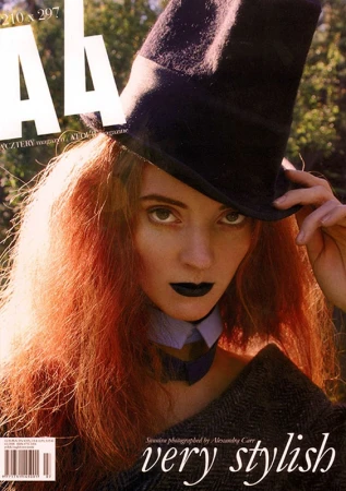 Close-up magazine cover featuring a woman with red hair wearing a top hat and dark lipstick with hair styled by Rebecca Plymate