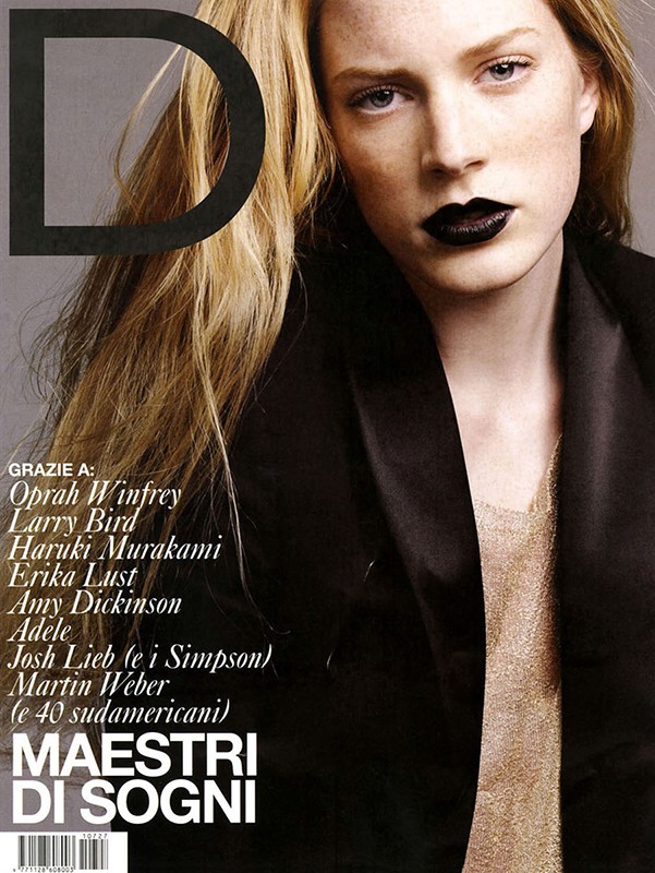 Fashion magazine cover featuring a blonde model with dark lipstick and a black blazer, posing in front of a gray background.