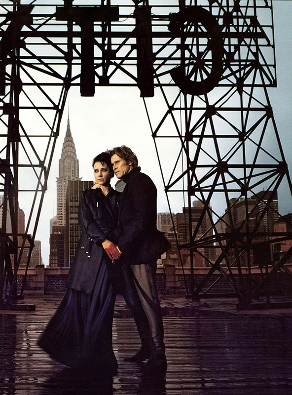Couple standing on a rooftop with the Chrysler Building in the background, under a metal structure spelling 'CITY'.