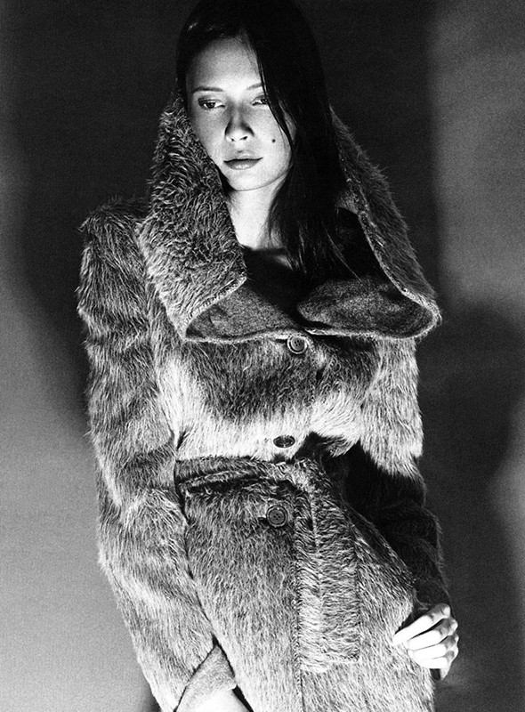 Monochrome studio portrait of an adult woman wearing a fur coat with a wide collar looking down with soft lighting. 
