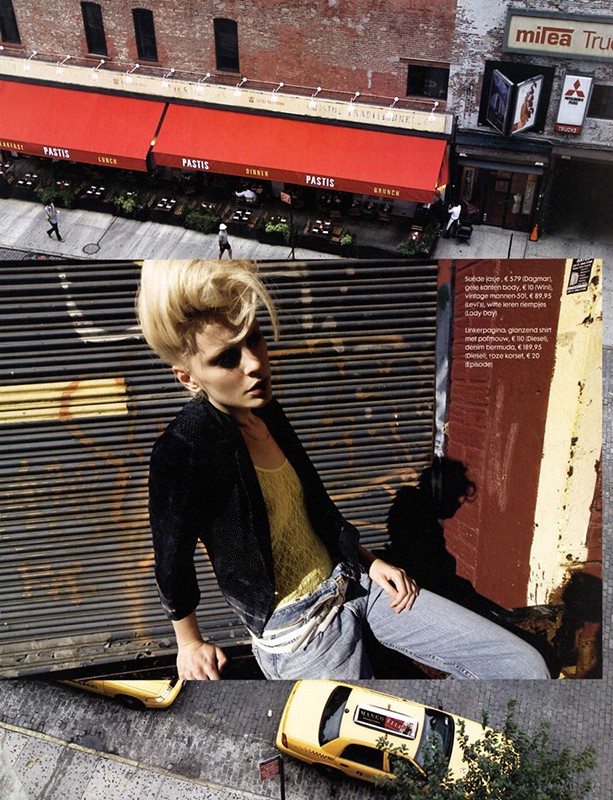 Fashion editorial shot. Woman with blonde hair poses next to a closed metal shutter, with a NYC taxi and building in the background.