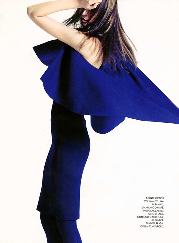 Fashion model in a vibrant blue dress poses in a studio against a white backdrop, showcasing modern minimalist couture.