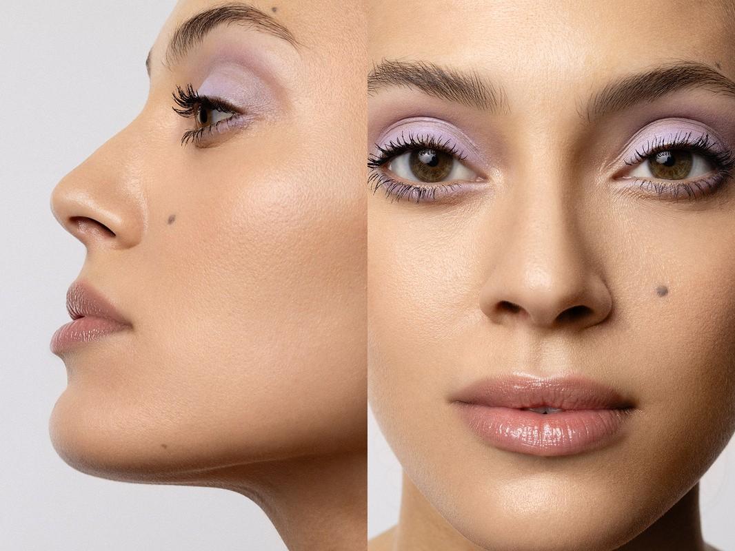 Close-up of a woman's face with light purple eyeshadow and glossy lips, captured in a beauty-style photograph with soft, neutral lighting.