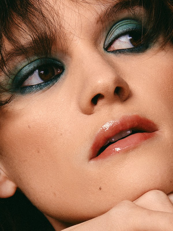 Close-up of a woman's face with striking teal eyeshadow and glossy lips, focusing on beauty and makeup in a studio setting.