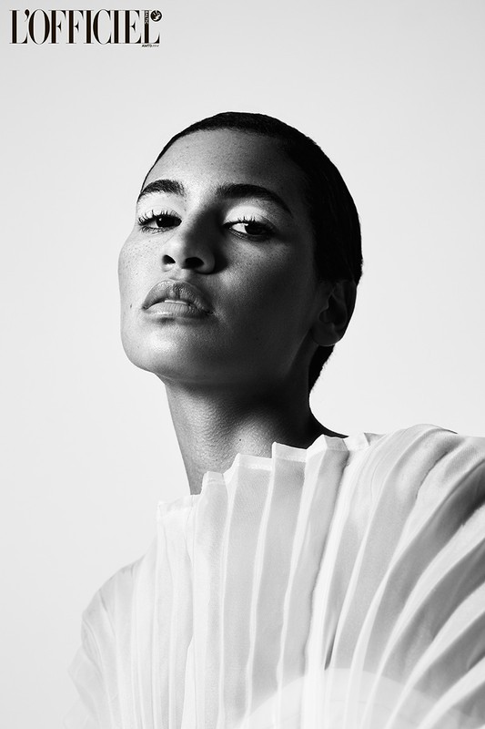 Black and white portrait of an adult woman with exaggerated makeup wearing a light, layered top against a neutral background.