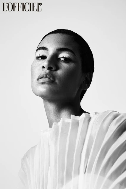Black and white portrait of an adult woman with exaggerated makeup wearing a light, layered top against a neutral background.