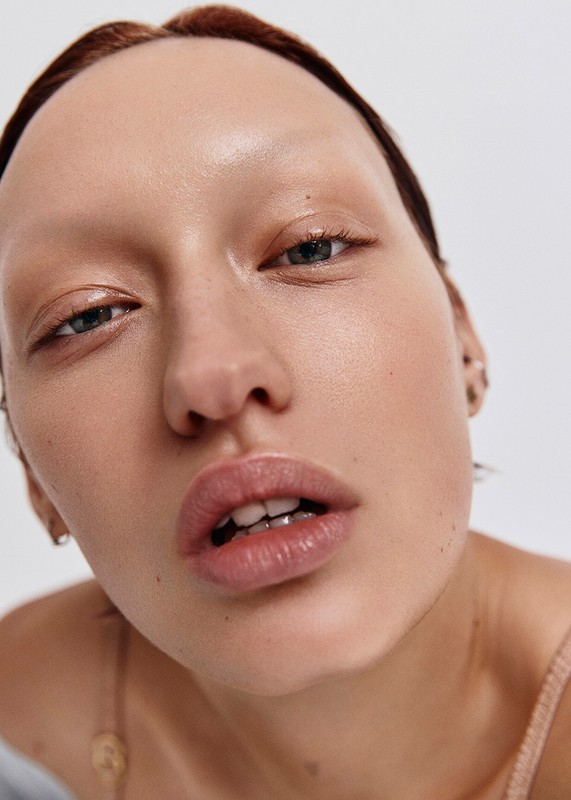 Close-up of a woman with fair skin, minimal makeup, and slightly parted lips, set against a stark white background.