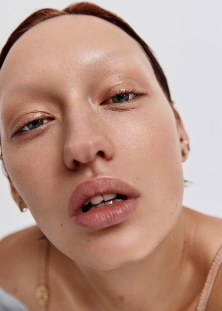 Close-up of a woman with fair skin, minimal makeup, and slightly parted lips, set against a stark white background.