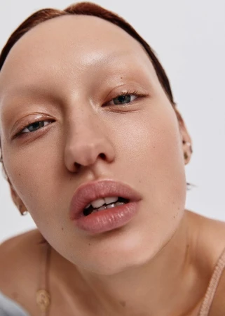 Close-up of a woman with fair skin, minimal makeup, and slightly parted lips, set against a stark white background.