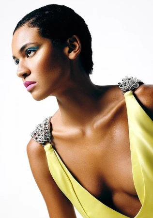 Elegant studio portrait of a Black woman in a yellow dress with jewel-encrusted straps against a bright white backdrop, showcasing fashion and beauty.
