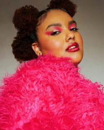 Close-up portrait of a woman with vibrant pink eyeshadow wearing a fluffy bright pink textured coat against a neutral background.