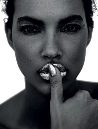 Close-up portrait of a woman with metallic silver lips and a finger touching her mouth against a bright white background
