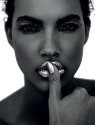 Close-up portrait of a woman with metallic silver lips and a finger touching her mouth against a bright white background