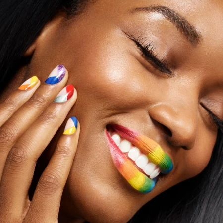 Close-up of a Black woman with closed eyes and colourful geometric nail art holding hand near her rainbow painted lips.