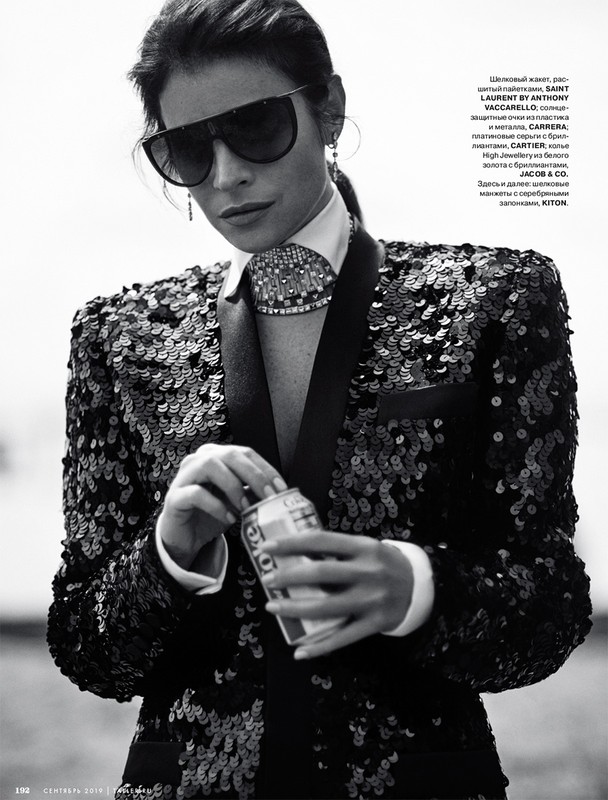 A striking black and white portrait of a stylish adult woman in a sequined jacket and oversized sunglasses, holding a can of soda.