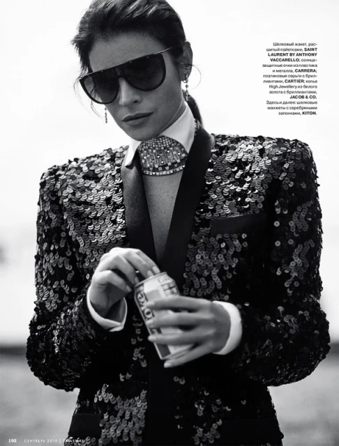 A striking black and white portrait of a stylish adult woman in a sequined jacket and oversized sunglasses, holding a can of soda.