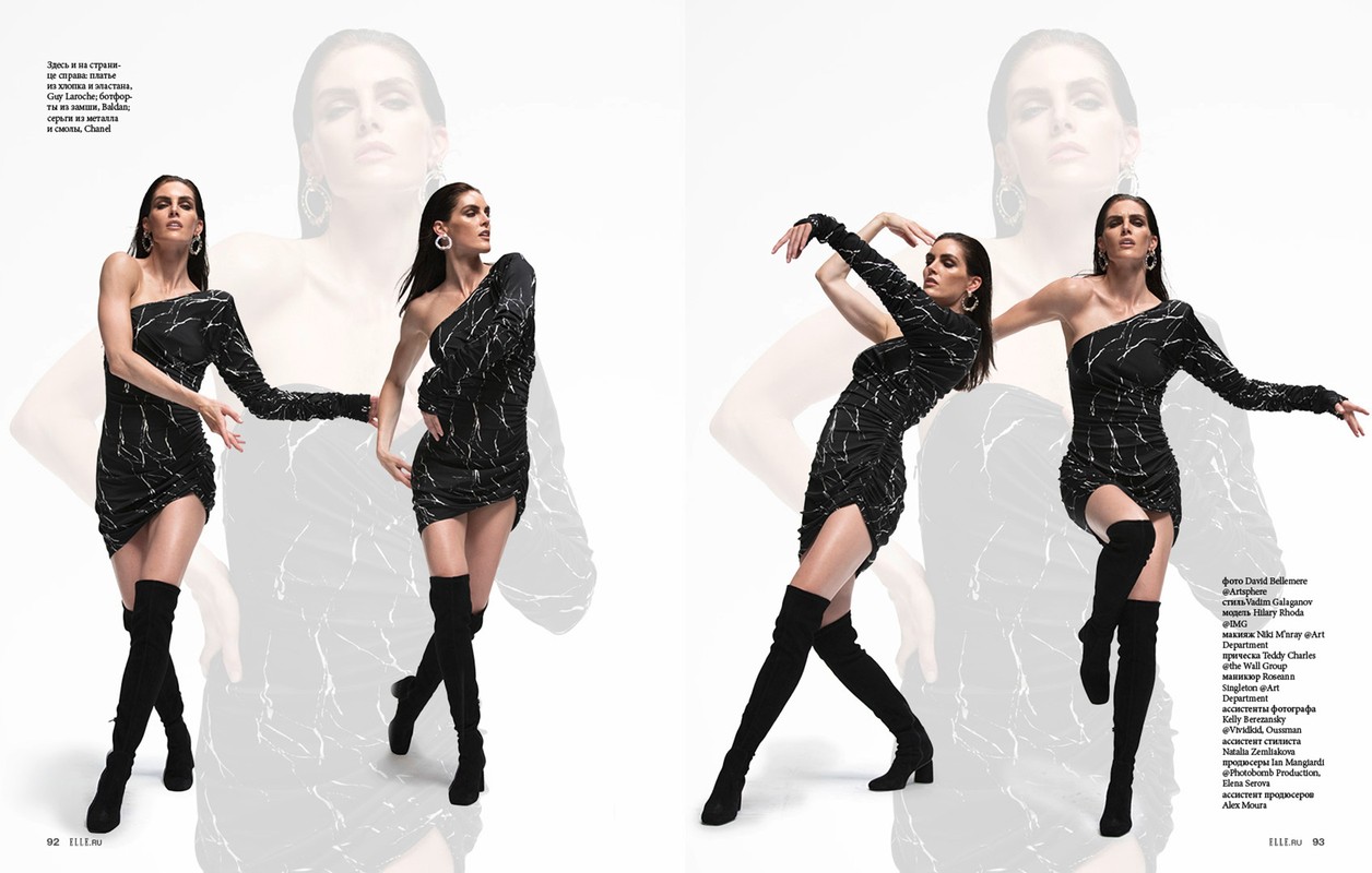 A model strikes a pose in a black one-shoulder mini dress and black thigh-high boots against a white backdrop with ghosted figures.