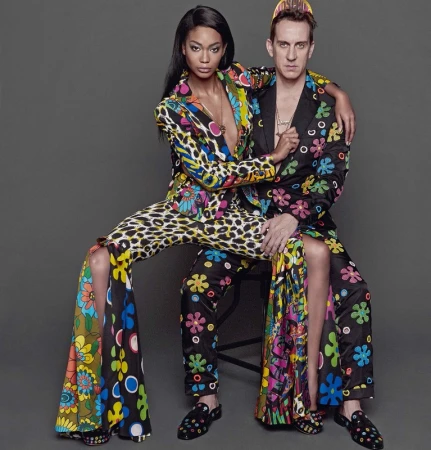 A fashion forward couple, one adult African American woman and one adult Caucasian man, pose in colorful floral and animal print suits.