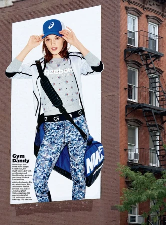 Advertisement featuring a female model in athletic wear against a brick building backdrop with fire escapes in an urban setting.