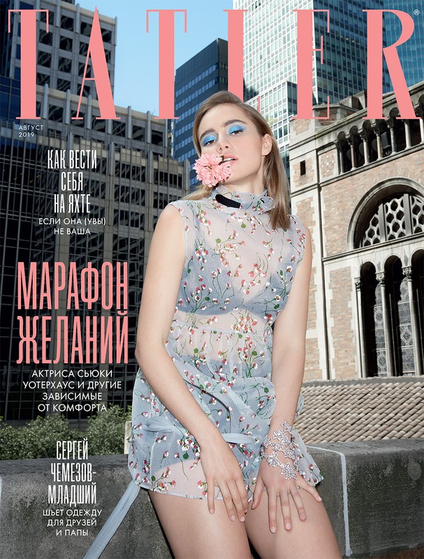 Magazine cover featuring a young woman in a floral dress with a pink flower in her mouth, set against a backdrop of urban buildings.
