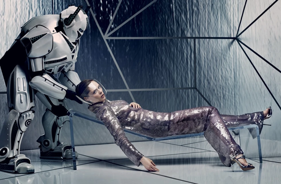 Woman in glittering outfit lies on chaise lounge with robot in futuristic, silvery interior; fashion, technology, beauty theme.