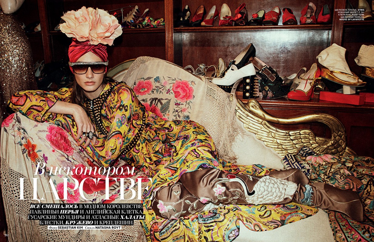 Fashion editorial image featuring a reclining female model in a yellow patterned dress, floral turban, and sunglasses amid vintage shoes.