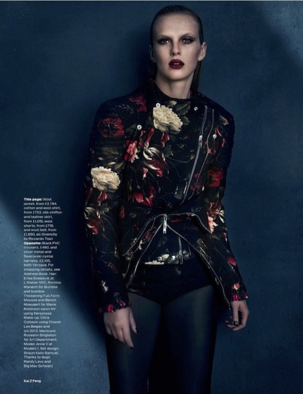 Fashion portrait of an adult woman in a floral moto jacket, dark lipstick, and slicked-back hair against a dark blue background.
