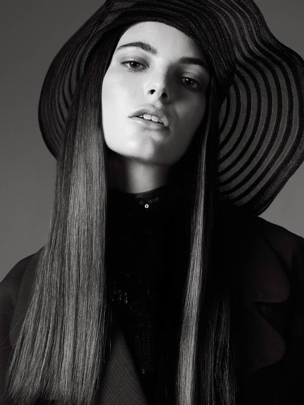 Portrait of a model with long straight hair wearing a wide-brimmed striped hat and black jacket in monochrome.