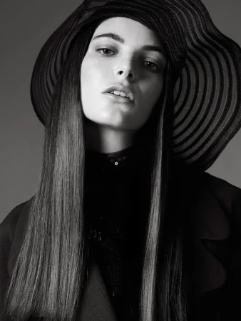 Portrait of a model with long straight hair wearing a wide-brimmed striped hat and black jacket in monochrome.