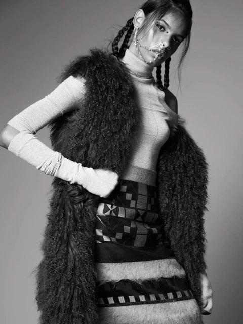 Monochrome fashion shot of a model wearing a fur vest, turtleneck, patterned skirt, and facial jewelry, posing in a photo studio.